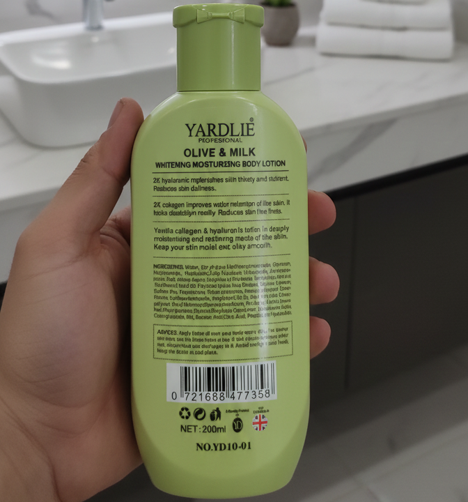 Hand holding a green bottle of Yardlie Olive & Milk Whitening Moisturizing Body Lotion in a bathroom setting.