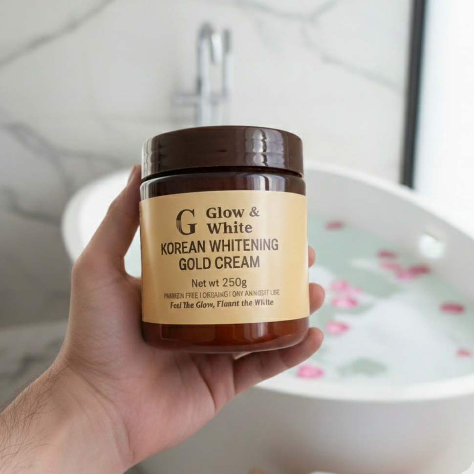Hand holding a jar of Glow & White Korean Whitening Gold Cream with a blurred bathroom background.